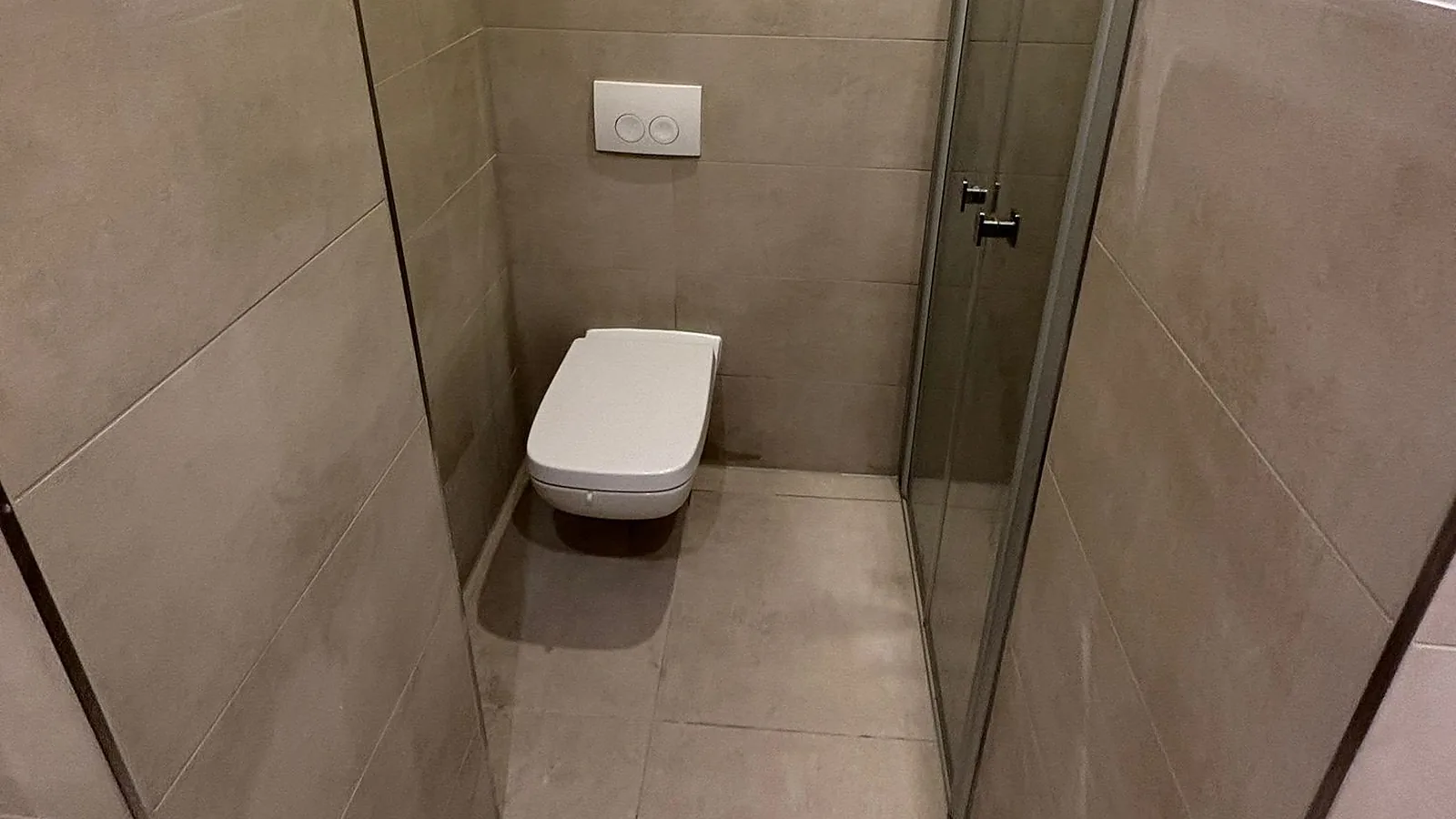Hängendes WC am Ende eines engen Raums, rechts eine Glastür