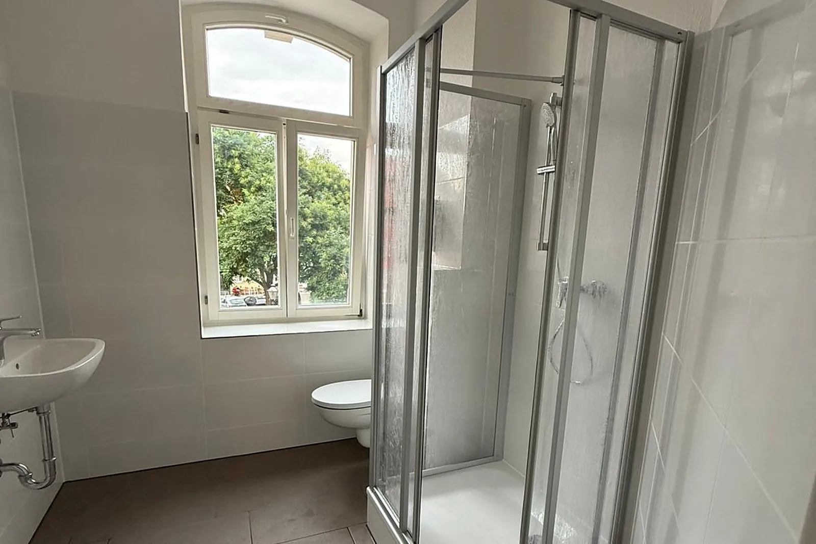 Renoviertes Altbaubad mit Rundbogenfenster, Duschkabine und Wand-WC